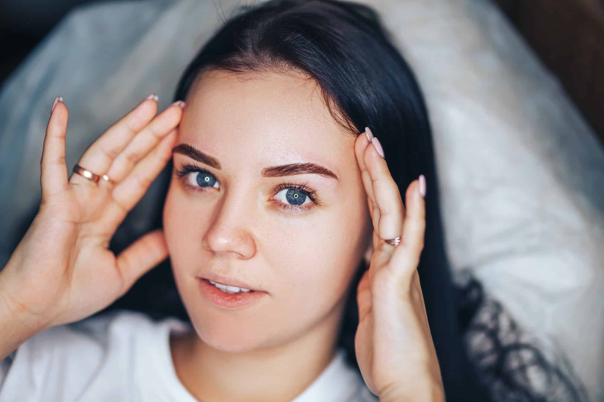 Young woman with beautiful eyebrows after procedure permanent make-up in salon, closeup photo